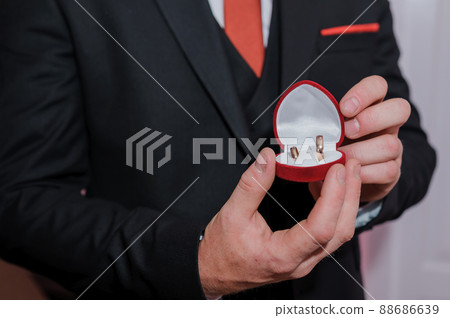 Red box with gold wedding rings in the hands of a man Red box with gold wedding rings in the hands of a man 88686639
