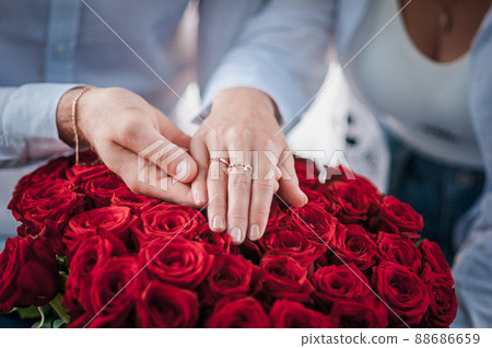 guy holds the girl's hand with a wedding ring over a bouquet of red roses 88686659