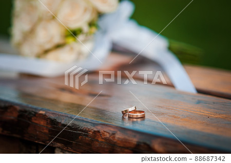 Wedding rings on a wooden stand against the background of the bride's bouquet 88687342