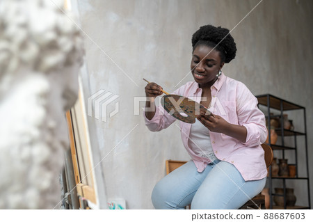A smiling dark-skinned artist mixing colors on palette 88687603