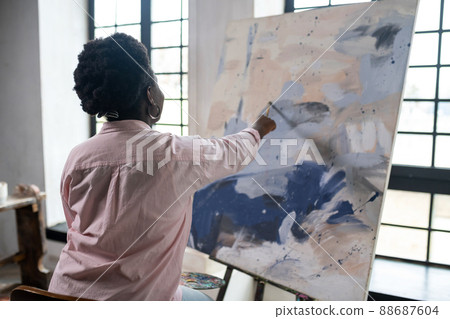 A dark-skinned woman sitting near the easel and painting 88687604