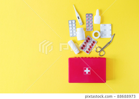 First aid kit red box with medical equipment and medications for emergency top view on pastel yellow background. 88688973