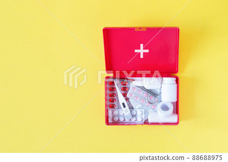 First aid kit red box with medical equipment and medications for emergency top view on pastel yellow background. 88688975