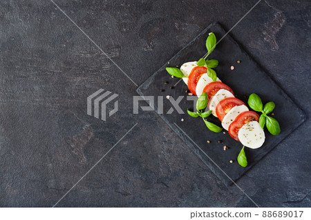 Caprese salad with mozzarela, tomatoes, fresh olive oil and basil on slate board on black background top view. Caprese salad with mozzarela, tomatoes, fresh olive oil and basil on slate board on black background top view. 88689017