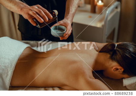 Masseur man therapist pouring warm herb infused oil to make back massage 88689238