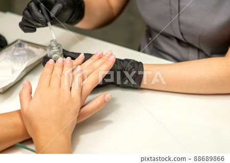 Manicure painting process. Manicure master paint the nails with transparent varnish in a nail salon, close up 88689866