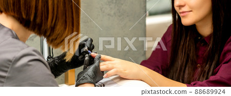Manicure master in rubber gloves applies an electric nail file to remove the nail polish in a nail salon Manicure master in rubber gloves applies an electric nail file to remove the nail polish in a nail salon 88689924