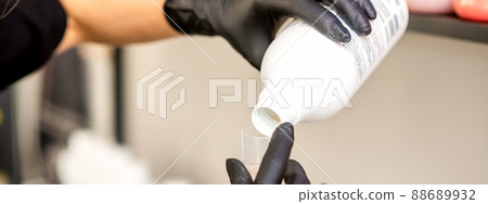 A hairdresser in black gloves is preparing hair dye with a bottle in a hair salon, close up A hairdresser in black gloves is preparing hair dye with a bottle in a hair salon, close up 88689932