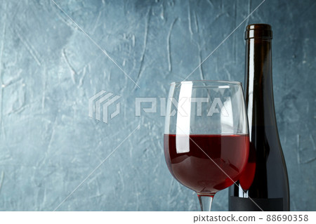 Bottle and glass of red wine against blue textured background 88690358