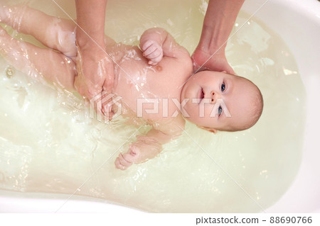 mother bathes her baby in a white small plastic tub mother bathes her baby in a white small plastic tub 88690766