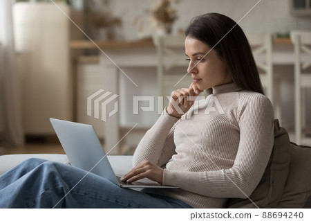 Thoughtful serious young laptop user woman relaxing on couch Thoughtful serious young laptop user woman relaxing on couch 88694240