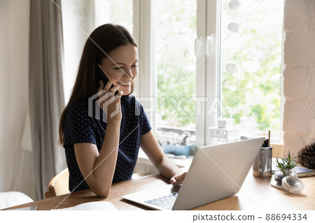 Woman sit at table with laptop enjoy conversation on cellphone Woman sit at table with laptop enjoy conversation on cellphone 88694334