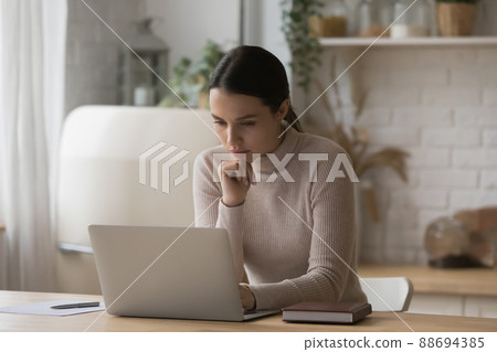 Thoughtful serious freelance worker woman working from home kitchen Thoughtful serious freelance worker woman working from home kitchen 88694385