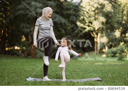 Muslim mother and her daughter, having workout in the park, doing high stepping exercise Muslim mother and her daughter, having workout in the park, doing high stepping exercise 88694539