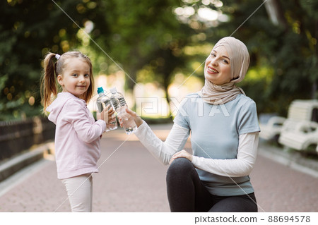 Muslim lady in hijab posing together with her cute little daughter with water bottles on camera Muslim lady in hijab posing together with her cute little daughter with water bottles on camera 88694578