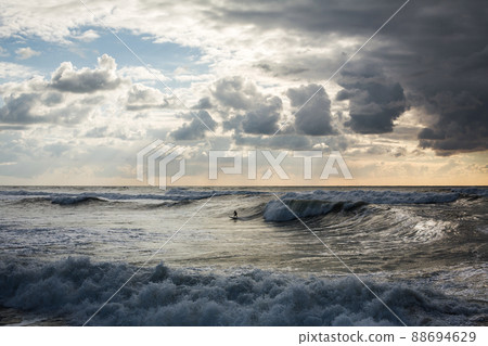 Surfers ride the sea waves at sunset Surfers ride the sea waves at sunset 88694629