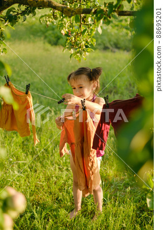 A little girl hangs clothes to dry after washing on a clothesline in nature in the fresh air. 88695201