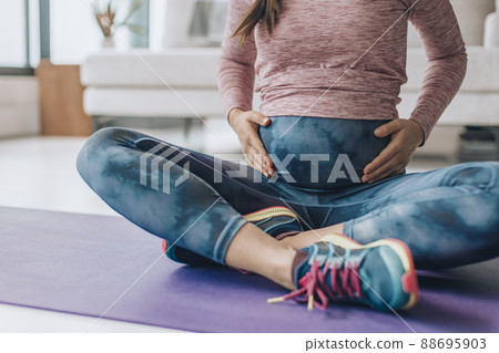 Activewear for pregnancy. Maternity clothes woman wearing full panel yoga leggings for bodyweight workout at home on floor mat Activewear for pregnancy. Maternity clothes woman wearing full panel yoga leggings for bodyweight workout at home on floor mat 88695903