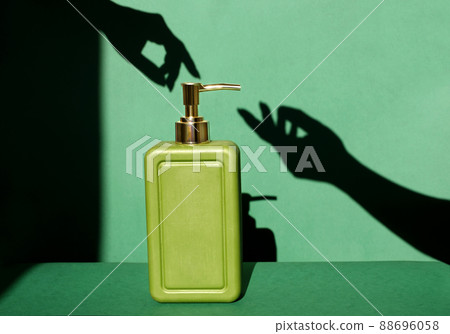A cosmetic product in a stylish green marble bottle with a golden dispenser and the shadow of elegant female hands on a studio background. Hand skin care with moisturizer and natural soap.Shades green A cosmetic product in a stylish green marble bottle with a golden dispenser and the shadow of elegant female hands on a studio background. Hand skin care with moisturizer and natural soap.Shades green 88696058