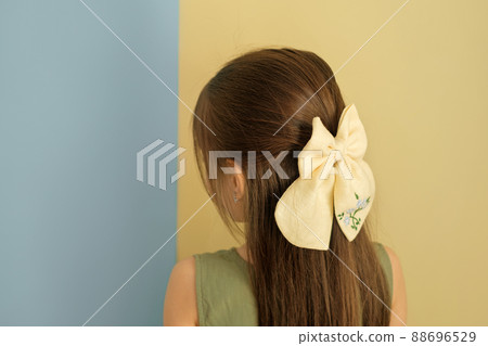 A beautiful big bow is an accessory for the hair on the girl's head. Long strong silky well-groomed brunette hair. A child on a yellow-blue studio background A beautiful big bow is an accessory for the hair on the girl's head. Long strong silky well-groomed brunette hair. A child on a yellow-blue studio background 88696529