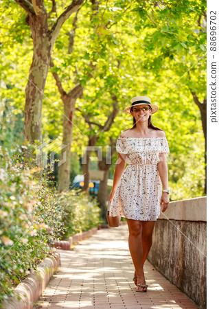 The bright beautiful girl in a light dress and hat walks along alley of trees in Monaco in sunny weather in the summer, handbag in hand The bright beautiful girl in a light dress and hat walks along alley of trees in Monaco in sunny weather in the summer, handbag in hand 88696702