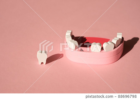 Wooden model of a human jaw with a missing tooth on a pink studio background. The problem of tooth loss. Baby milk teeth. 88696798