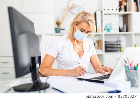 Woman in disposable mask working in business office using laptop 88703327