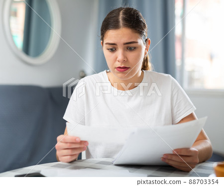 Upset woman with financial documents sitting at the table 88703354
