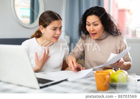 Two women with financial documents near laptop sitting at table at home Two women with financial documents near laptop sitting at table at home 88703569