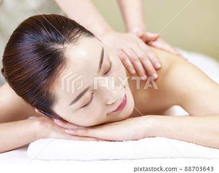 close-up of face of a beautiful young asian woman lying on front on bed receiving massage in spa salon close-up of face of a beautiful young asian woman lying on front on bed receiving massage in spa salon 88703643