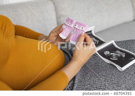 Pregnant woman looking at ultrasound scan gender reveal showing its a baby girl holding newborn pink socks awaiting the birth of her child. First trimester pregnancy 88704391