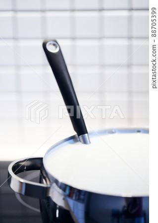 The process of making yogurt. Milk is heated and fermented by bacteria. Milk in a pot on the stove. Vertical photo. 88705399