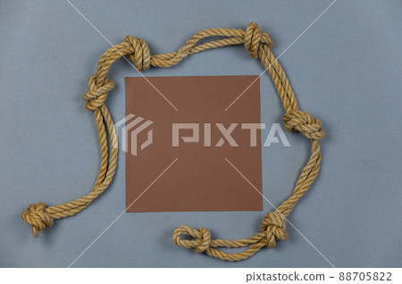 A ship's rope with knots and a brown empty square against a gray background. Top view 88705822