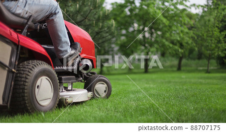 Lawn mower with driver mowing the grass on a green meadow. Copy space Lawn mower with driver mowing the grass on a green meadow. Copy space 88707175