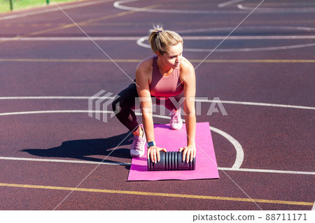 Motivated determined fit woman training on mat outdoor summer day, doing plank crunch abs exercise with foam roller, alternating knee workout. Warm-up before sports activity, health care concept 88711171