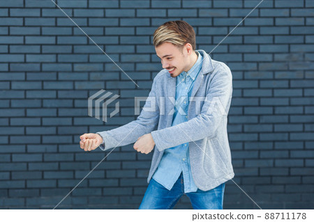 Profile side view portrait of attentive handsome young blonde man in casual style standing in pulling gesture or boxing attack. indoor studio shot on brick wall background. 88711178