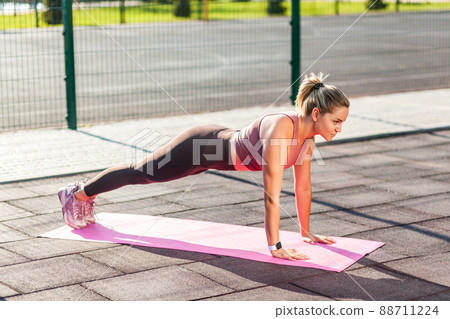 Full length, fit beautiful woman in tight pants practicing yoga on mat outdoor summer day, doing perfect plank asana, phalankasana pose and looking serious motivated. Health care, sports activity 88711224