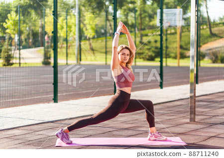Motivated fit athletic woman in tight pants practicing yoga on mat outdoor summer day, standing in Virabhadrasana warrior pose and meditating, doing stretching exercise. Health care, sport activity Motivated fit athletic woman in tight pants practicing yoga on mat outdoor summer day, standing in Virabhadrasana warrior pose and meditating, doing stretching exercise. Health care, sport activity 88711240