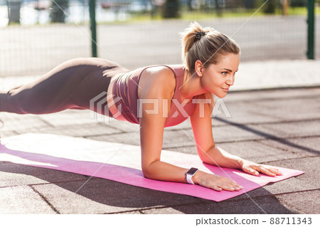 side view, strong fit girl in tight pants training on mat outdoor summer day, doing perfect plank exercise and looking motivated, concentrated on pilates workout. Health care, sport activity 88711343