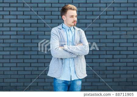 Portrait of serious calm handsome young blonde man in casual style standing with crossed arms and looking away with relaxed face. indoor studio shot on brick wall background. Portrait of serious calm handsome young blonde man in casual style standing with crossed arms and looking away with relaxed face. indoor studio shot on brick wall background. 88711905