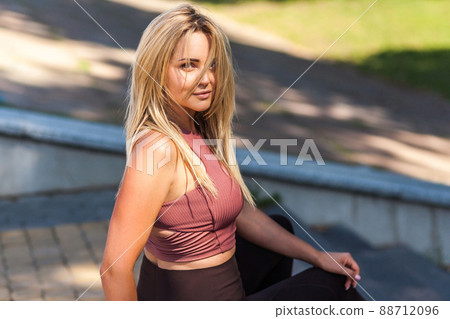 Sexy attractive woman in sportswear sitting on stairs outdoor and looking seductively at camera, her clean healthy young skin and long blond hair illuminated by sun. Concept of female beauty, fashion Sexy attractive woman in sportswear sitting on stairs outdoor and looking seductively at camera, her clean healthy young skin and long blond hair illuminated by sun. Concept of female beauty, fashion 88712096