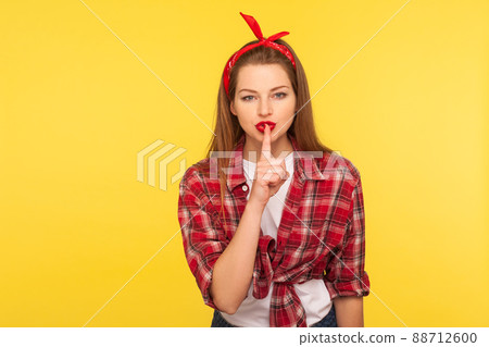 Shh, don't tell secret. Portrait of sexy pinup girl in checkered shirt and headband keeping finger on red lips showing silence gesture, looking seductively. retro 50's style, studio shot isolated Shh, don't tell secret. Portrait of sexy pinup girl in checkered shirt and headband keeping finger on red lips showing silence gesture, looking seductively. retro 50's style, studio shot isolated 88712600