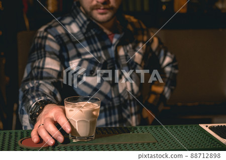 Bartender offering iced cocktail with cream and coffee liqueur on bar counter 88712898