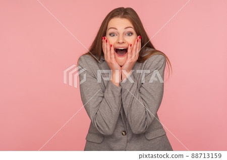 Portrait of amazed young brunette woman in business suit keeping hands on face and shouting in surprise, expressing genuine astonishment, shock reaction. indoor studio shot isolated on pink background Portrait of amazed young brunette woman in business suit keeping hands on face and shouting in surprise, expressing genuine astonishment, shock reaction. indoor studio shot isolated on pink background 88713159