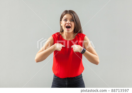 Portrait of shocked beautiful brunette young woman in red shirt standing, pointing herself and looking at camera with amazed surprised face. indoor, studio shot, isolated on gray background. Portrait of shocked beautiful brunette young woman in red shirt standing, pointing herself and looking at camera with amazed surprised face. indoor, studio shot, isolated on gray background. 88713597