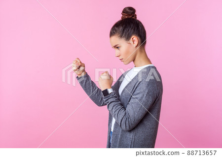 Side view of brave teenage girl with bun hairstyle in casual clothes standing in defensive posture with raised fists, ready to punch, looking aggressive and confident. studio shot, pink background Side view of brave teenage girl with bun hairstyle in casual clothes standing in defensive posture with raised fists, ready to punch, looking aggressive and confident. studio shot, pink background 88713657