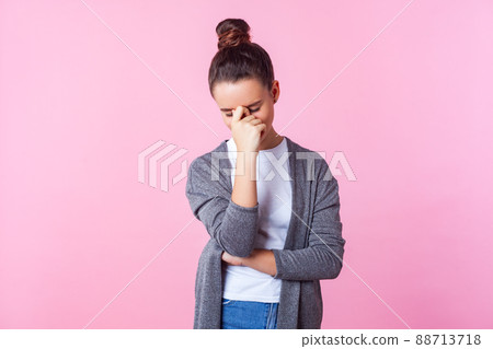Portrait of upset brunette teenage girl with bun hairstyle in casual clothes hiding face in hand crying, feeling stressed worried, suffering headache. indoor studio shot isolated on pink background Portrait of upset brunette teenage girl with bun hairstyle in casual clothes hiding face in hand crying, feeling stressed worried, suffering headache. indoor studio shot isolated on pink background 88713718