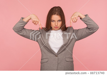 Here and right now. Portrait of strict angry brunette lady boss in business suit pointing down, demanding to come immediately, leader ordering and controlling. studio shot isolated on pink background Here and right now. Portrait of strict angry brunette lady boss in business suit pointing down, demanding to come immediately, leader ordering and controlling. studio shot isolated on pink background 88713740