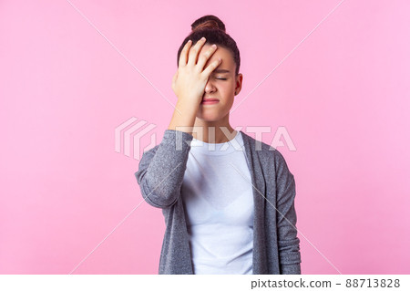Facepalm, oh no. Portrait of unhappy teen girl with bun hairstyle in casual clothes standing with hand on head, feeling sorrow regret blaming herself for failure. studio shot isolated, pink background Facepalm, oh no. Portrait of unhappy teen girl with bun hairstyle in casual clothes standing with hand on head, feeling sorrow regret blaming herself for failure. studio shot isolated, pink background 88713828