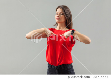 Portrait of proud satisfied beautiful brunette young woman in red shirt standing, pointing herself, looking at camera with confident face. indoor, studio shot, isolated on gray background. Portrait of proud satisfied beautiful brunette young woman in red shirt standing, pointing herself, looking at camera with confident face. indoor, studio shot, isolated on gray background. 88714535